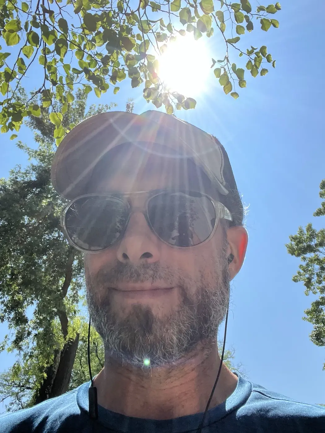 Michael Eric West outdoors beneath a bright summer sun, wearing a cap and sunglasses.