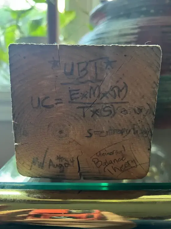 The original wooden phone stand bearing Michael’s handwritten early Universal Balance Theory equation and the words S equals entropy flow.
